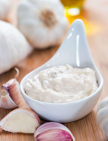 Serving of garlic aioli surrounded by garlic bulbs and cloves.