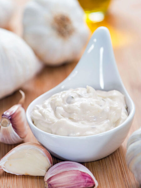 Serving of garlic aioli surrounded by garlic bulbs and cloves.