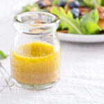 Apple cider vinaigrette in a clear bottle with a green salad.