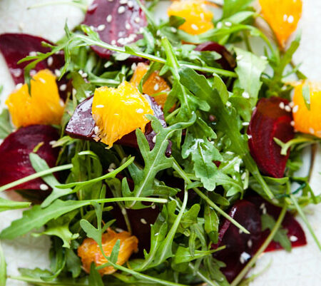 arugula salad with beets, orange, and toasted sesame seeds on a plate.
