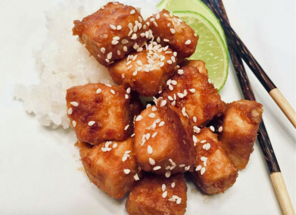 Baked peanut tofu with rice, a wedge of lime, and chopsticks