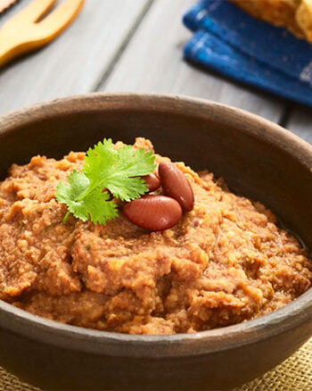 Bowl of bean dip with background of utensils and bread.