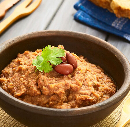 Bowl of bean dip with background of utensils and bread.