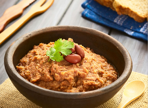 Bowl of bean dip with background of utensils and bread.