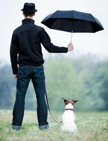 Young man holding an umbrella over his dog.