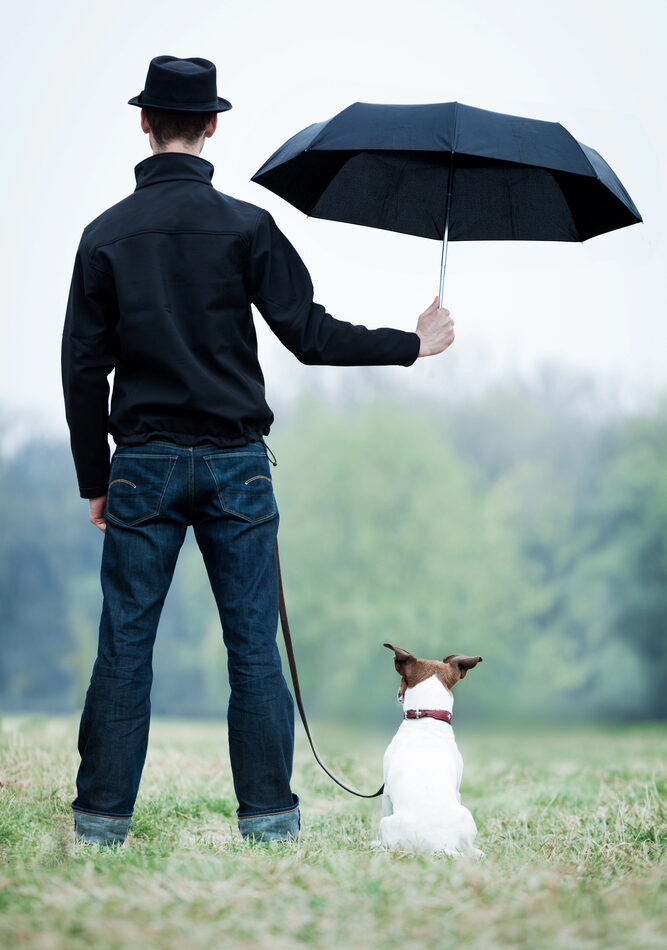 Young man holding an umbrella over his dog.