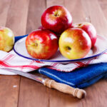 Apples sitting on a towel next to a sharp knife.