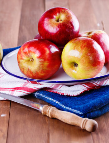 Apples sitting on a towel next to a sharp knife.