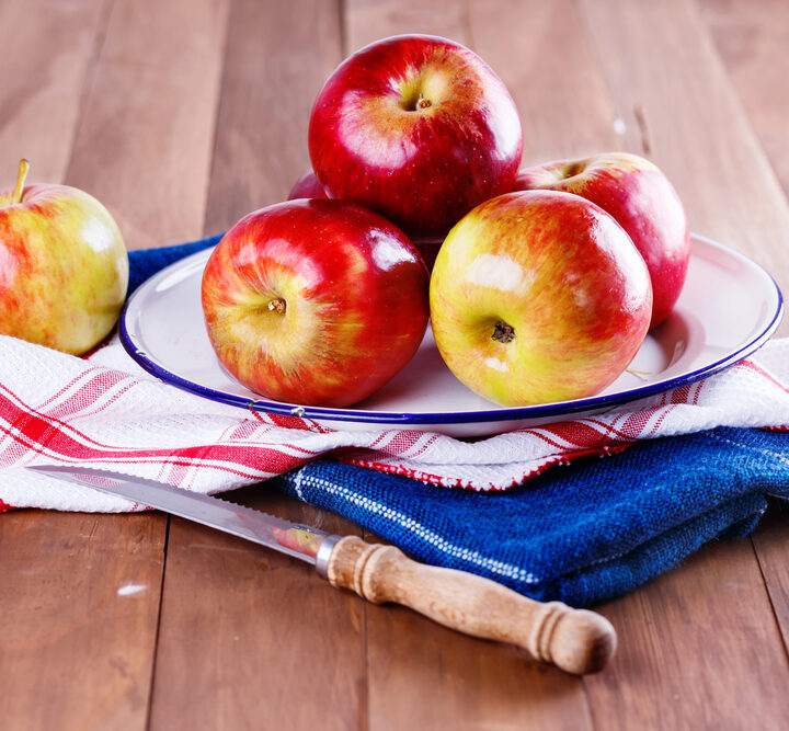 Apples sitting on a towel next to a sharp knife.