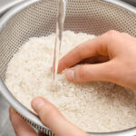Woman rinsing rice in sifter under running water, closeup