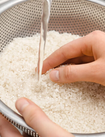 Woman rinsing rice in sifter under running water, closeup