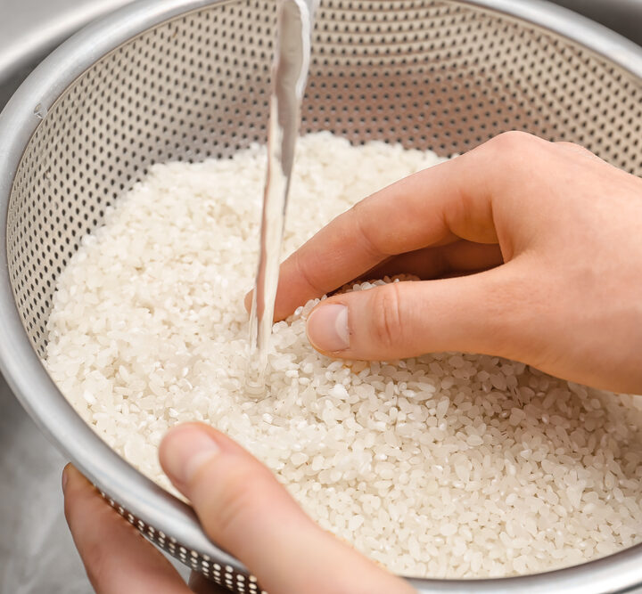 Woman rinsing rice in sifter under running water, closeup