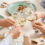 Four friends toasting with wine glasses over a dinner table.
