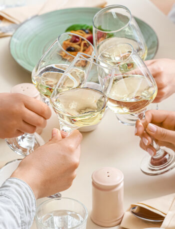 Four friends toasting with wine glasses over a dinner table.