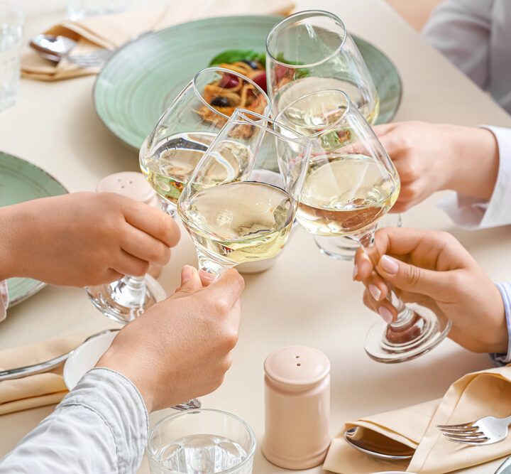 Four friends toasting with wine glasses over a dinner table.