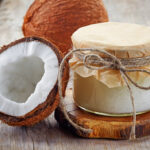 A halved coconut sitting next to a jar of coconut oil.