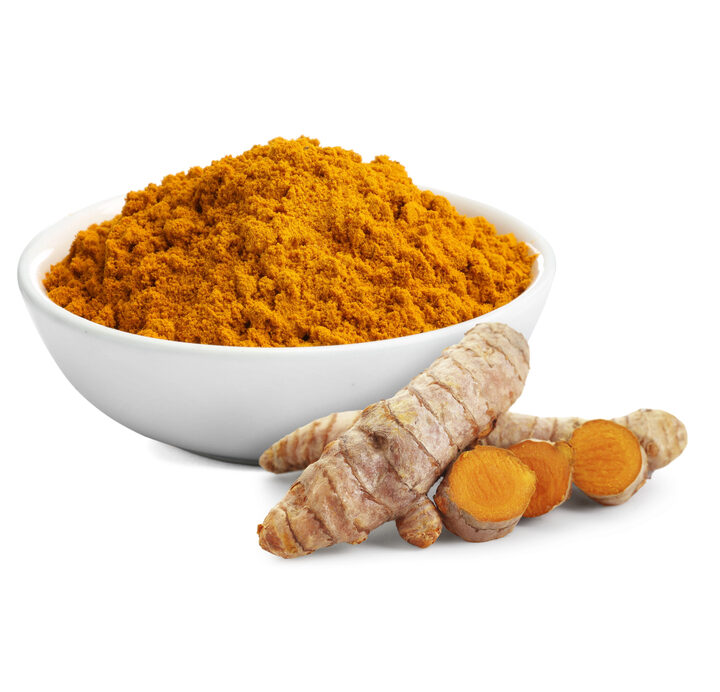 Fresh turmeric root next to a bowl of turmeric powder.