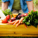 Person kneeling behind a bin filled with vegetables.