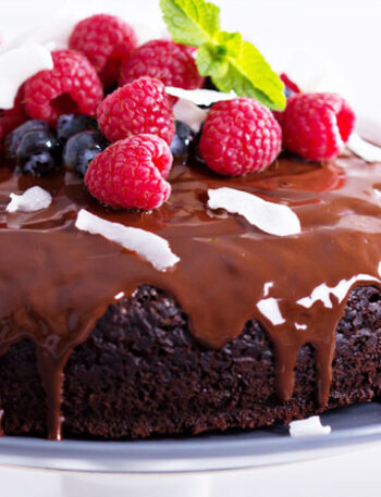 Delectable chocolate cake topped with berries and shredded coconut on a cake plate.