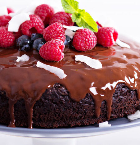Delectable chocolate cake topped with berries and shredded coconut on a cake plate.