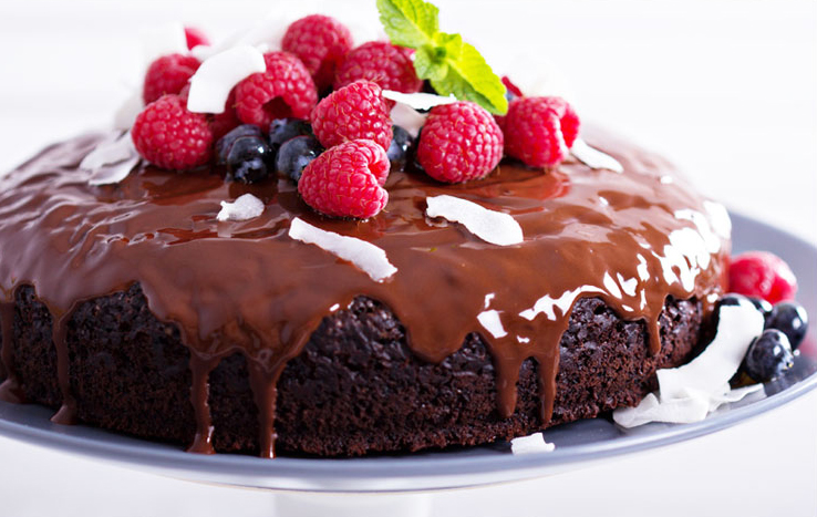 Delectable chocolate cake topped with berries and shredded coconut on a cake plate.