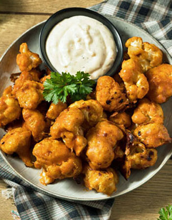 Plated roasted buffalo cauliflower wings with ranch dressing and parsley garnish sitting on a checkered napkin.