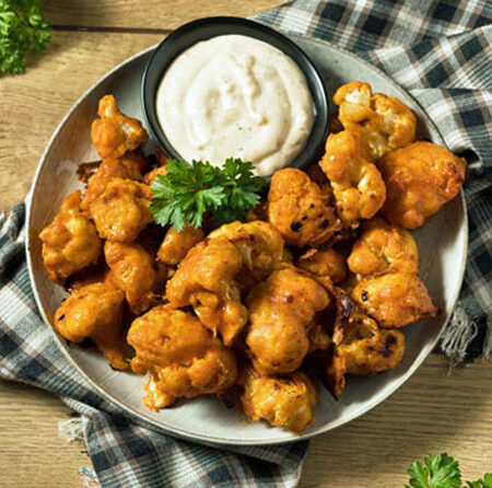 Plated roasted buffalo cauliflower wings with ranch dressing and parsley garnish sitting on a checkered napkin.