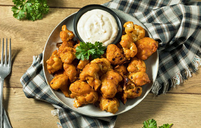 Plated roasted buffalo cauliflower wings with ranch dressing and parsley garnish sitting on a checkered napkin.
