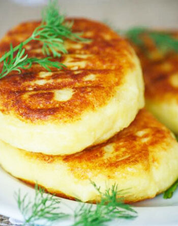 Three potato cakes on a white plate with a dill garnish.
