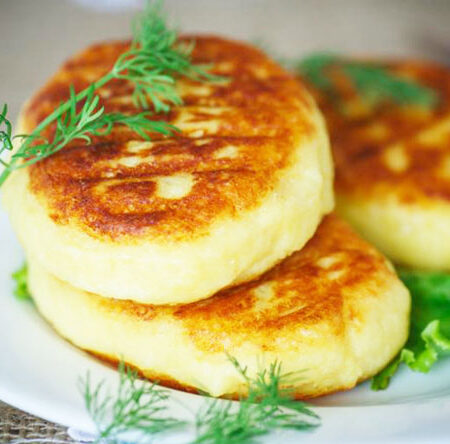 Three potato cakes on a white plate with a dill garnish.