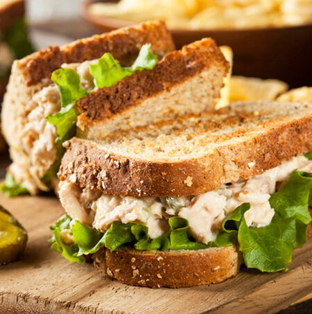 Toasted tuna fishless sandwich with lettuce and pickle on a wooden cutting board.