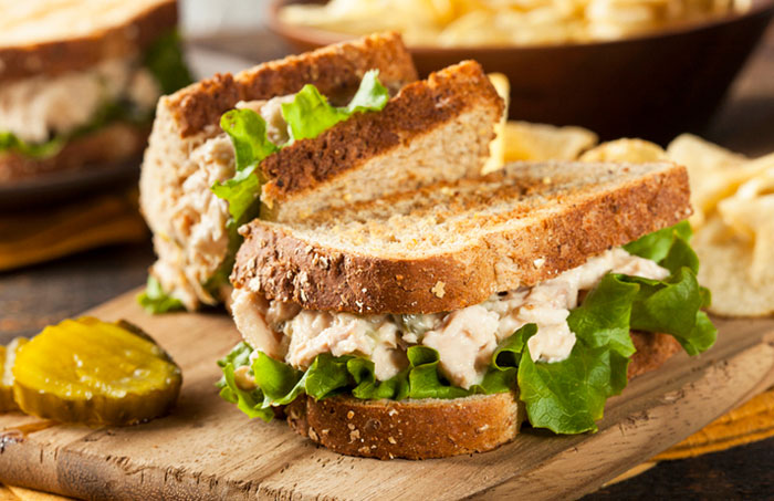 Toasted tuna fishless sandwich with lettuce and pickle on a wooden cutting board.