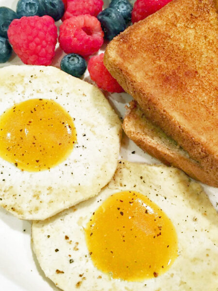 Two vegan fried eggs, toast, and berries on a breakfast plate.