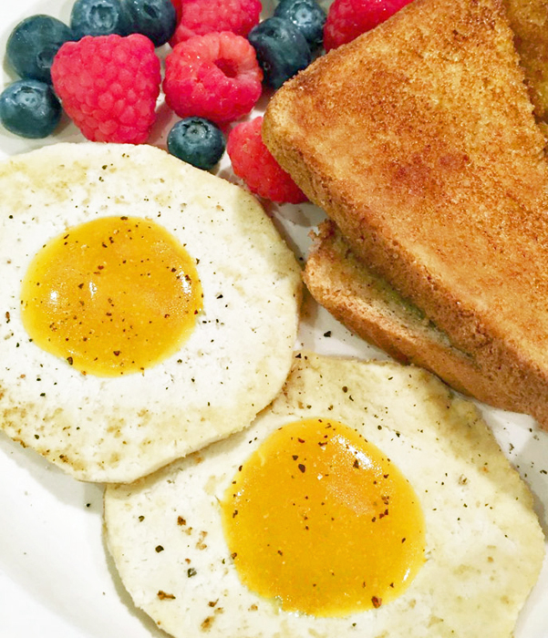 Two vegan fried eggs, toast, and berries on a breakfast plate.