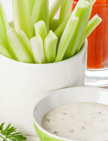 Cups of celery and carrots next to a bowl of vegetable dip.