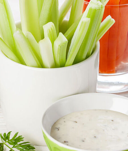 Cups of celery and carrots next to a bowl of vegetable dip.