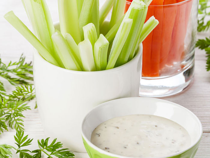 Cups of celery and carrots next to a bowl of vegetable dip.