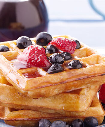 Vegan waffles with blueberries, strawberries, and maple syrup, plated on a blue napkin.
