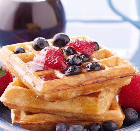 Vegan waffles with blueberries, strawberries, and maple syrup, plated on a blue napkin.