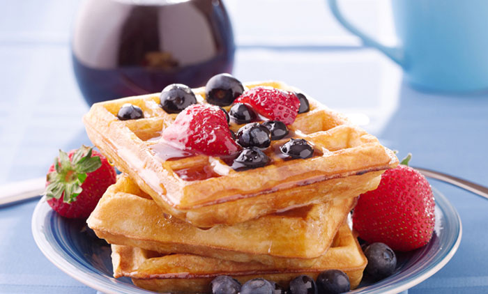 Vegan waffles with blueberries, strawberries, and maple syrup, plated on a blue napkin.