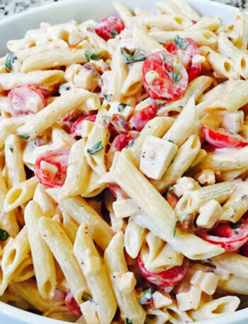 Zesty pasta salad with tomatoes, basil, and smoked gouda in a white bowl.
