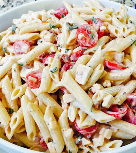 Zesty pasta salad with tomatoes, basil, and smoked gouda in a white bowl.