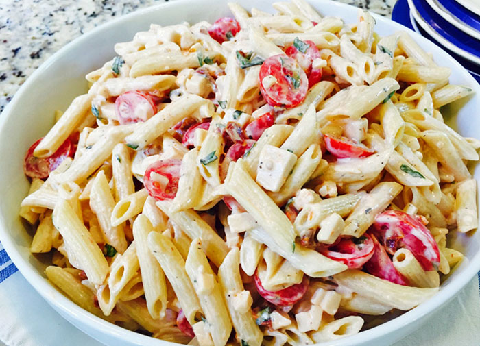 Zesty pasta salad with tomatoes, basil, and smoked gouda in a white bowl.