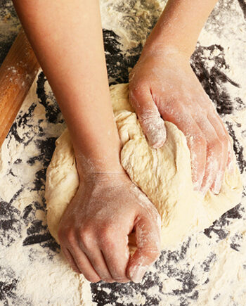 A woman's hands kneading dough on a floured surface next to a rolling pin.