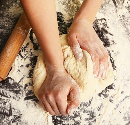 A woman's hands kneading dough on a floured surface next to a rolling pin.