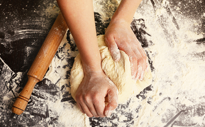 A woman's hands kneading dough on a floured surface next to a rolling pin.