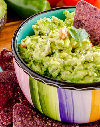 Homemade Hawaiian Guacamole dip in a colorful bowl with blue corn chips.