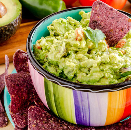 Homemade Hawaiian Guacamole dip in a colorful bowl with blue corn chips.
