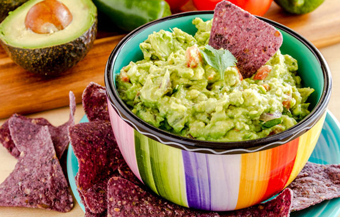 Homemade Hawaiian Guacamole dip in a colorful bowl with blue corn chips.