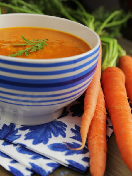 Blue and white striped bowl filled with Curried Carrot Soup, and fresh carrots beside it.